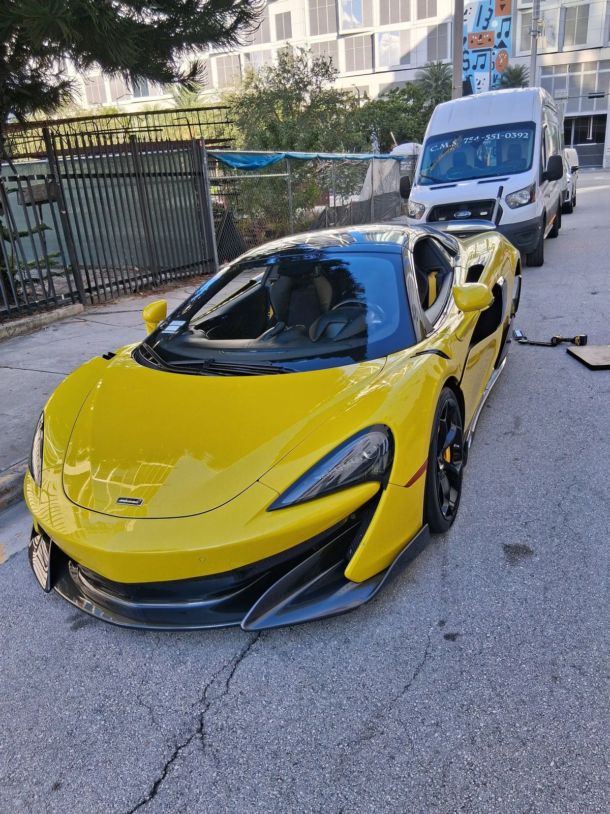 Yellow McLaren parked at the curb with the white service van behind it