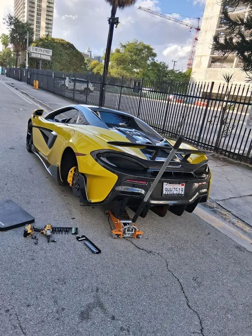 Yellow McLaren raised on a jack in the street with a wheel off