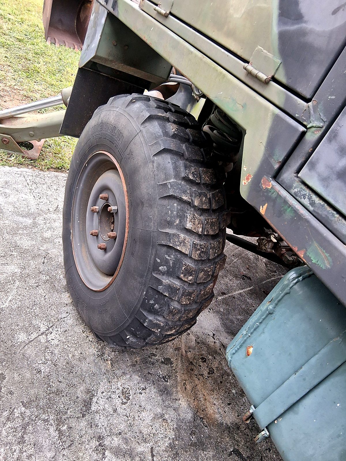 Camouflage military truck with a large knobby tire being worked on