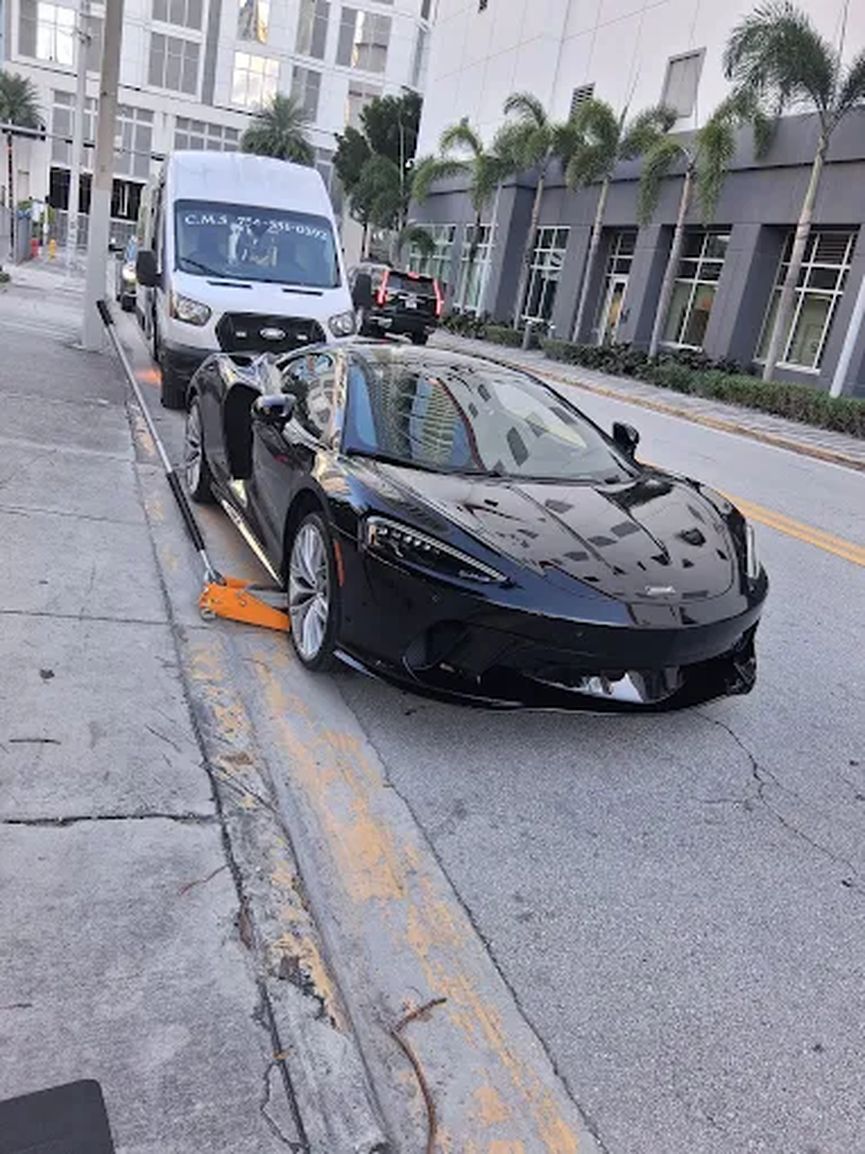 Black sports car at the curb with the service van parked behind it