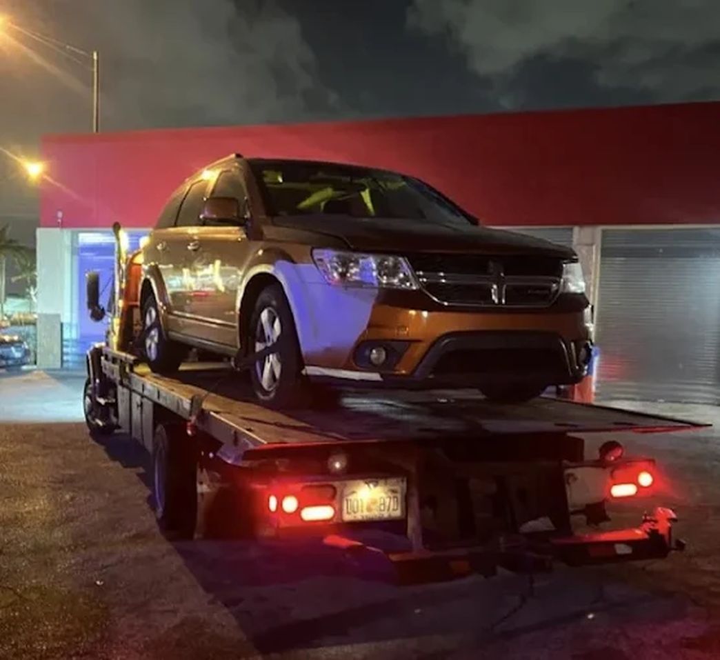 Orange SUV loaded on a flatbed tow truck at night