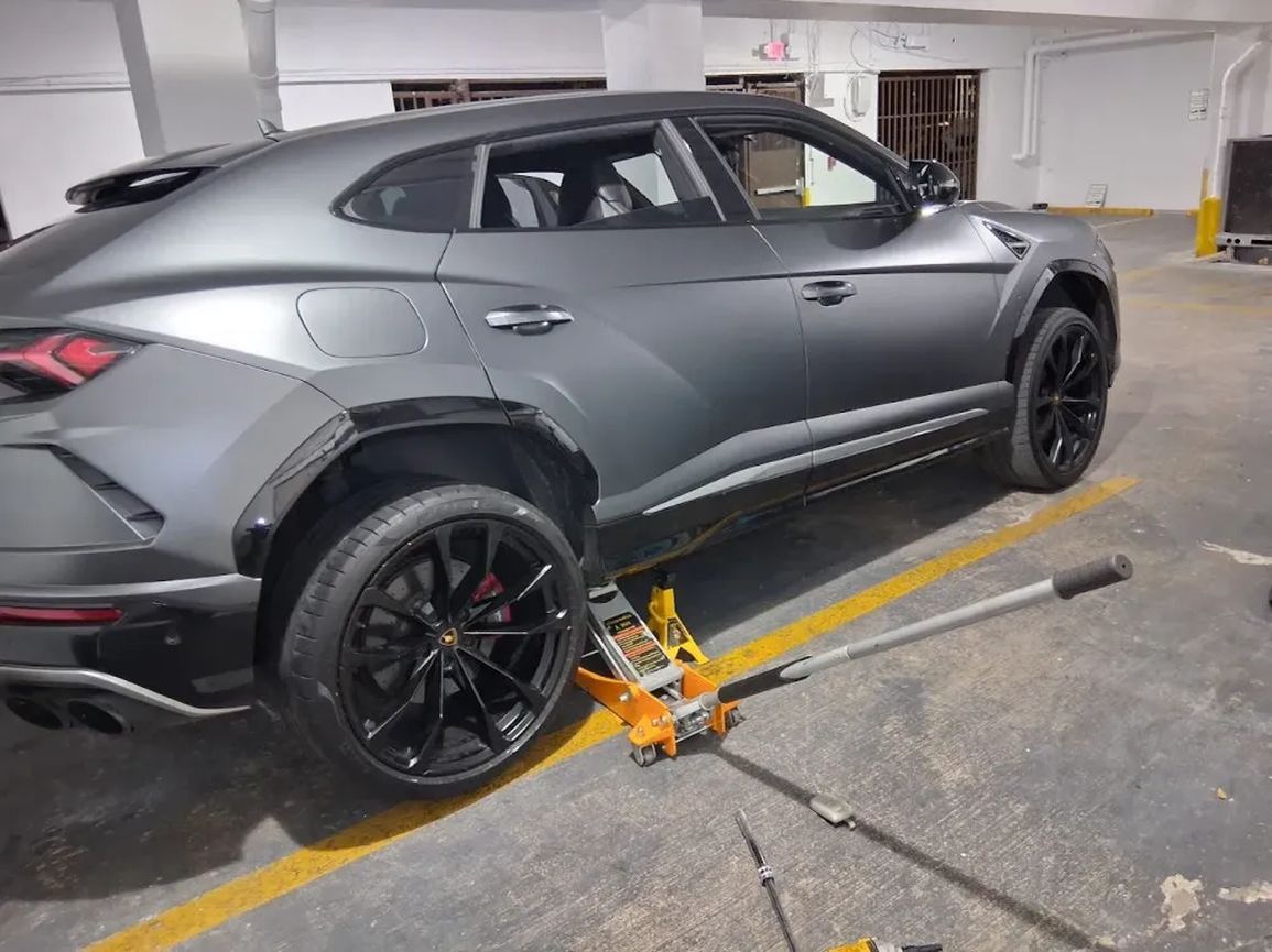 Grey Lamborghini Urus lifted on a floor jack with a wheel off