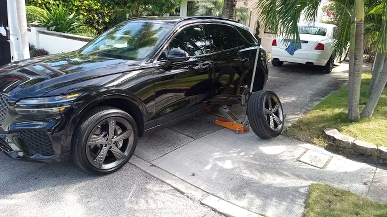Black car on a jack with the wheel removed, parked on a lawn